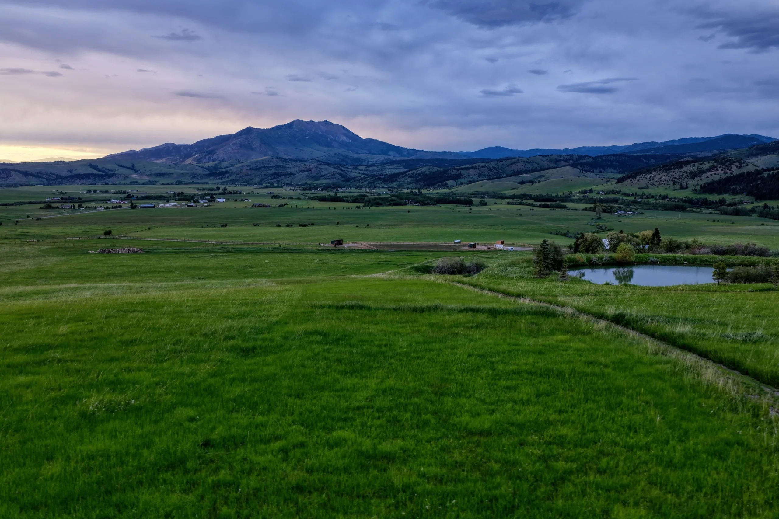 Green meadow and pond below the mountains at dusk